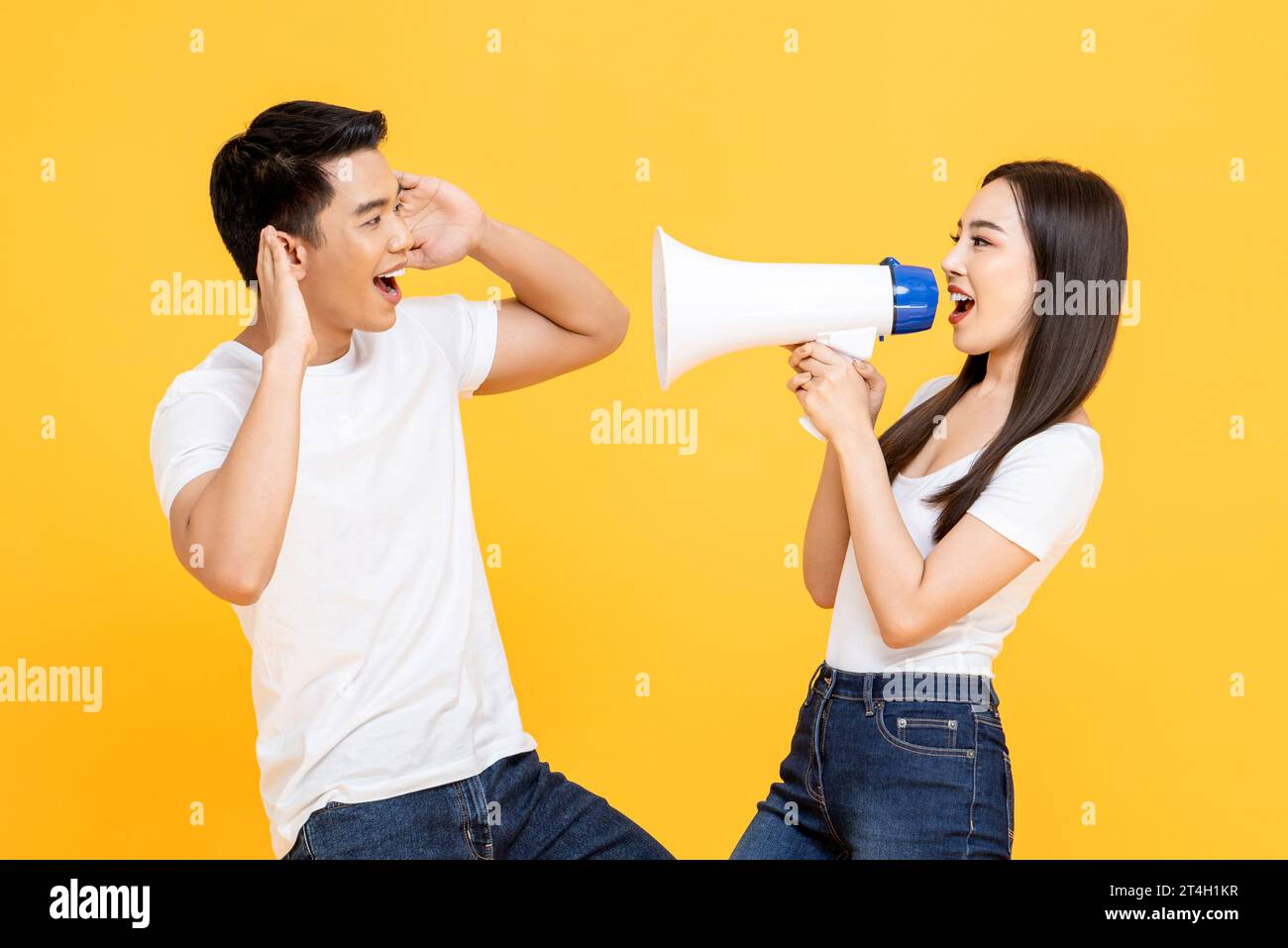Jeune femme asiatique parlant sur mégaphone à son petit ami en studio isolé fond de couleur jaune Banque D'Images