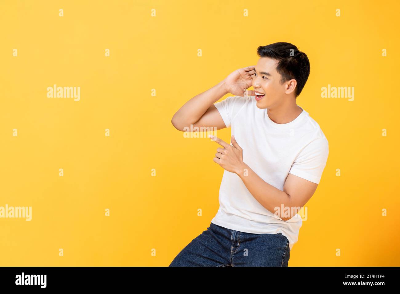 Souriant jeune homme asiatique joyeux regardant et pointant sur le côté dans le fond jaune isolé du studio Banque D'Images