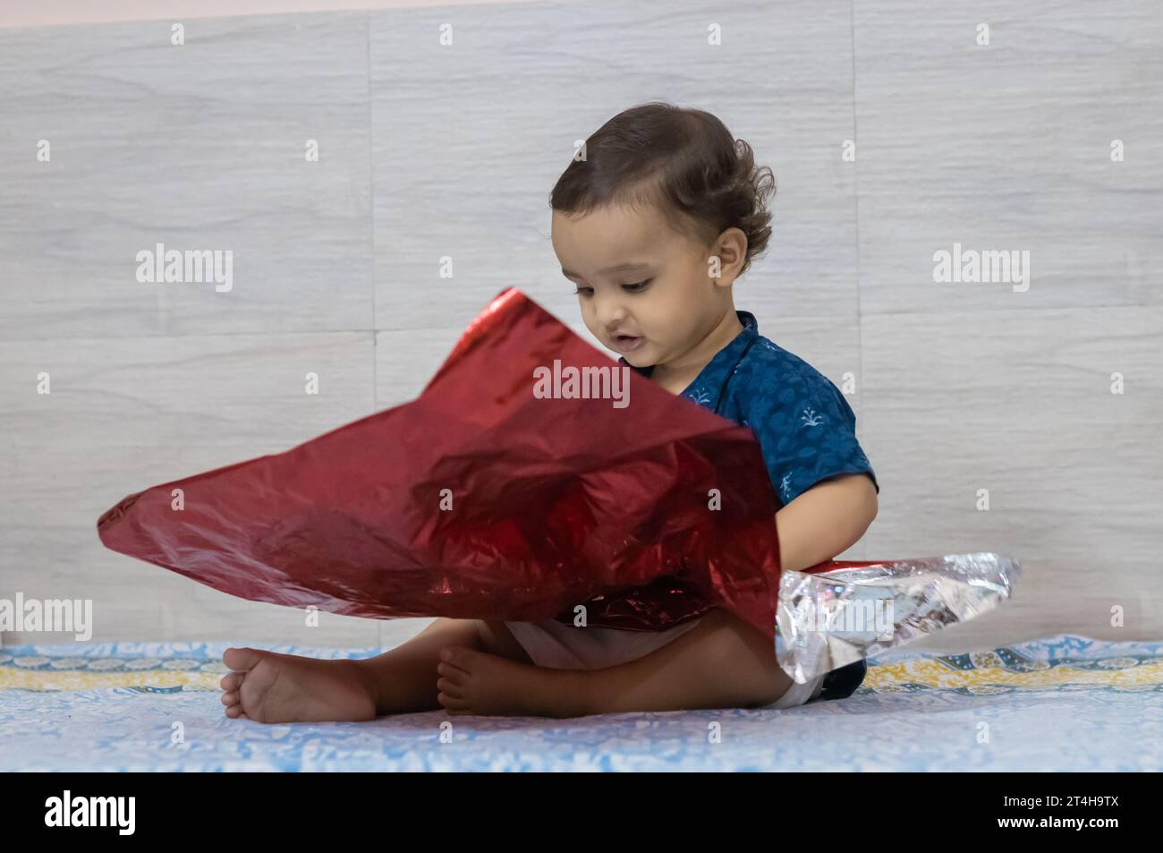 mignon bébé garçon en bas âge jouant avec le papier de déformation de couleur rouge à l'intérieur Banque D'Images