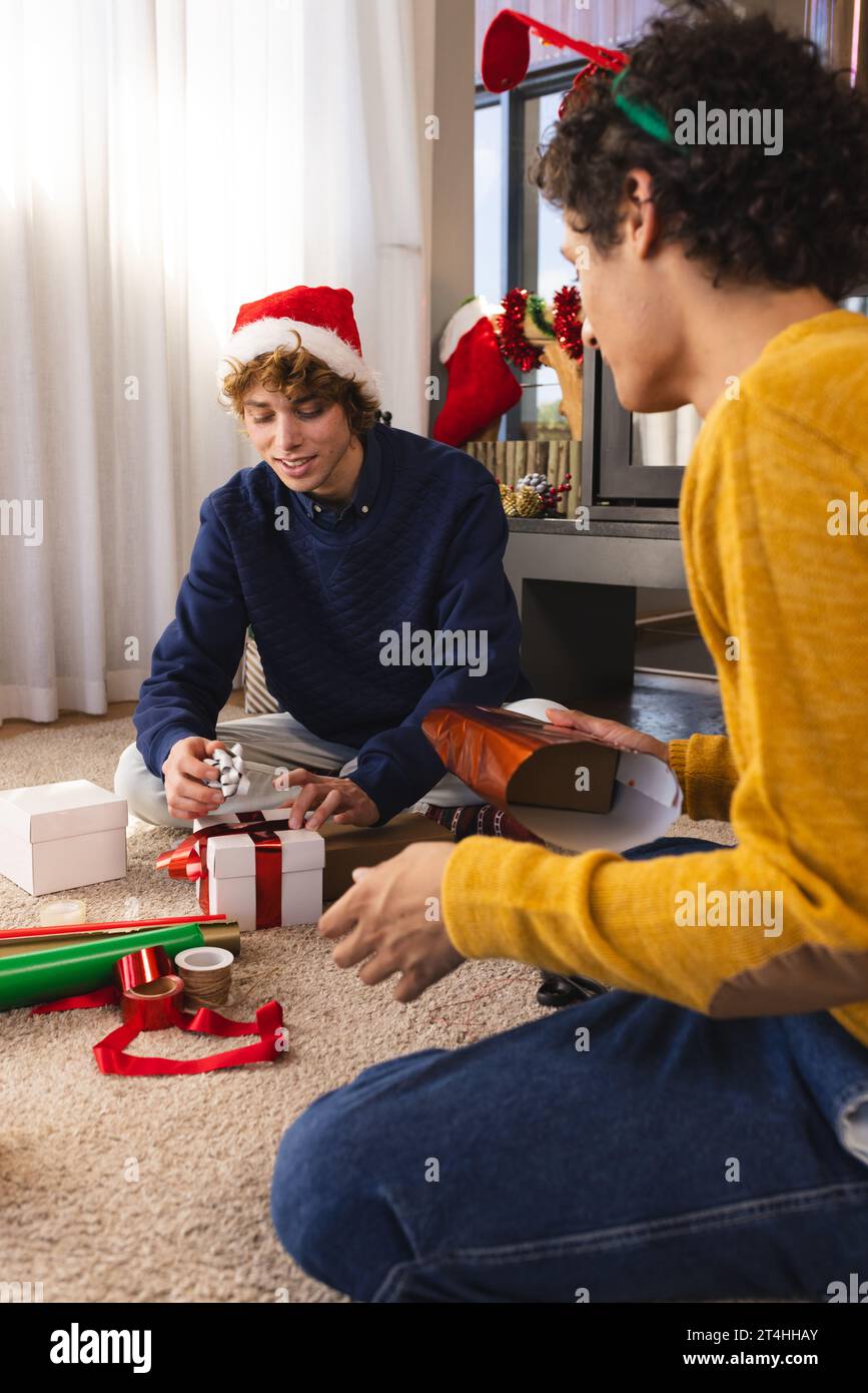 Heureux couple masculin gay diversifié portant des chapeaux de noël et des cadeaux d'emballage à la maison Banque D'Images