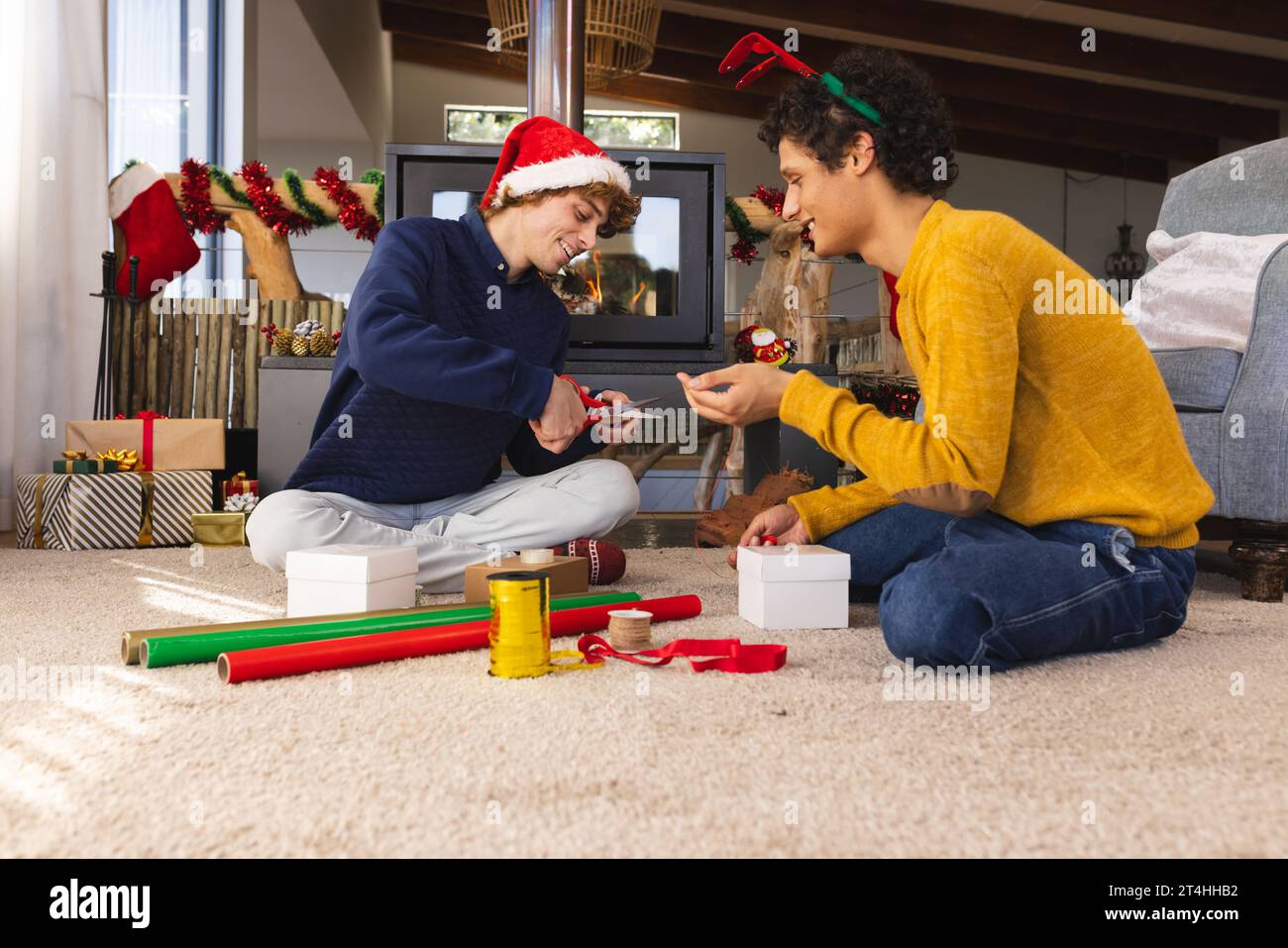 Heureux couple masculin gay diversifié portant des chapeaux de noël et des cadeaux d'emballage à la maison Banque D'Images
