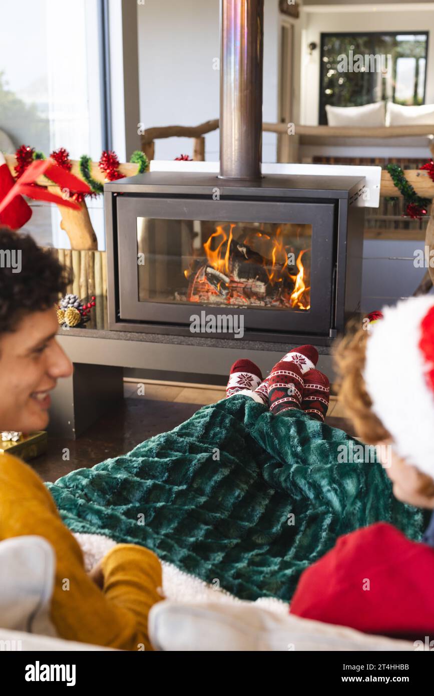 Heureux couple masculin gay diversifié parlant et portant des vêtements de noël à la maison Banque D'Images