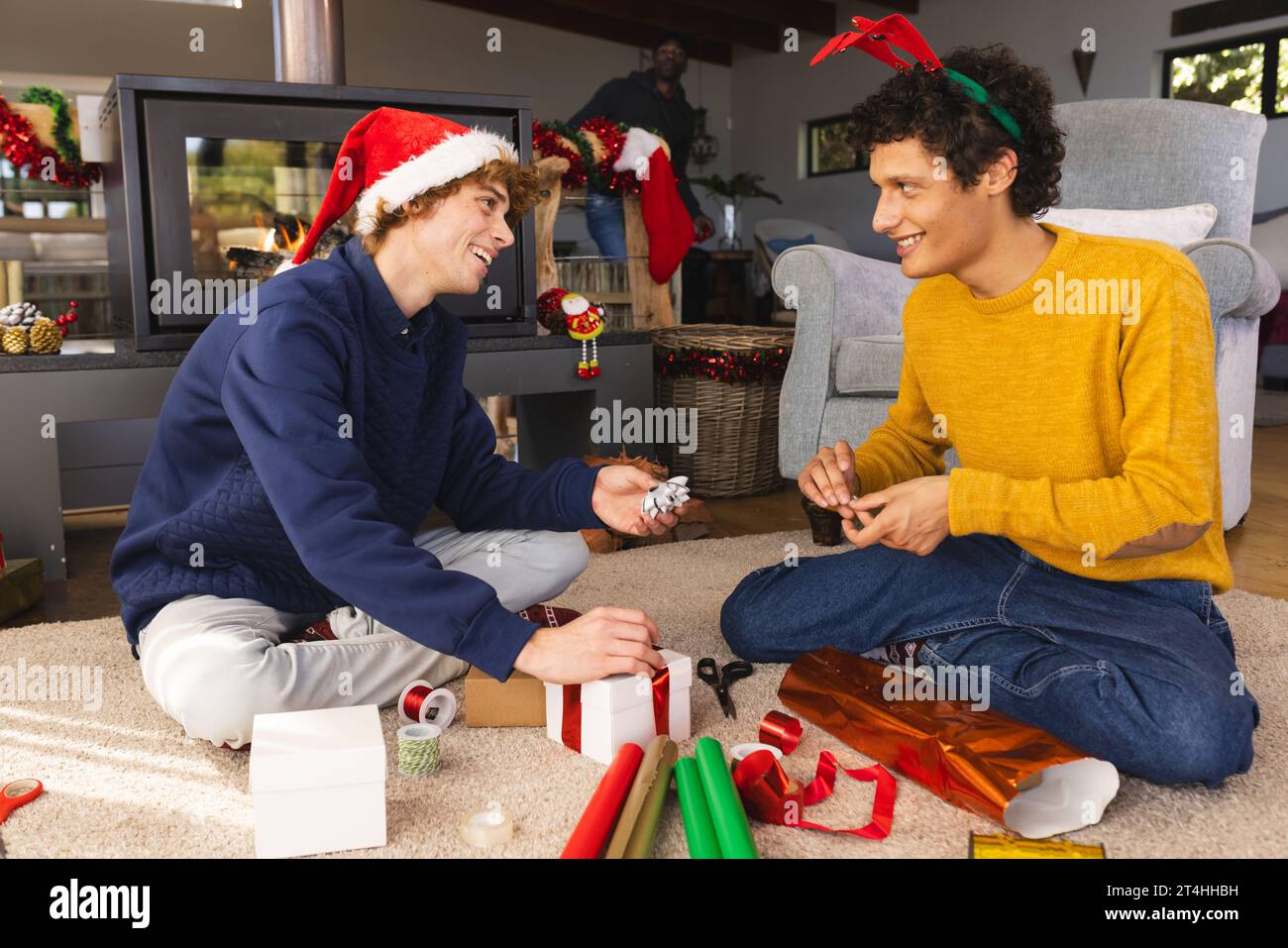 Heureux couple masculin gay diversifié portant des chapeaux de noël et des cadeaux d'emballage à la maison Banque D'Images