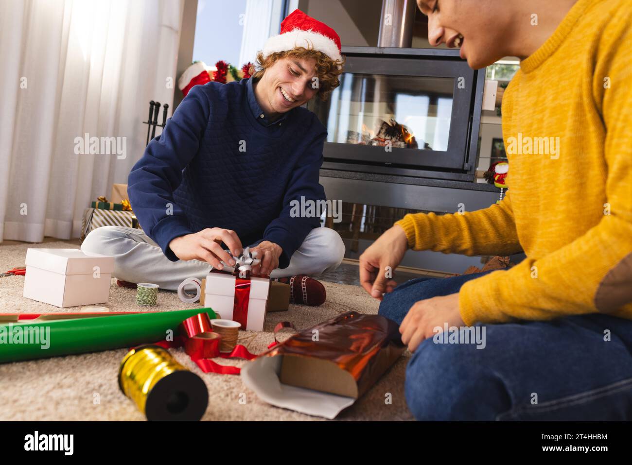 Heureux couple masculin gay diversifié portant des chapeaux de noël et des cadeaux d'emballage à la maison Banque D'Images
