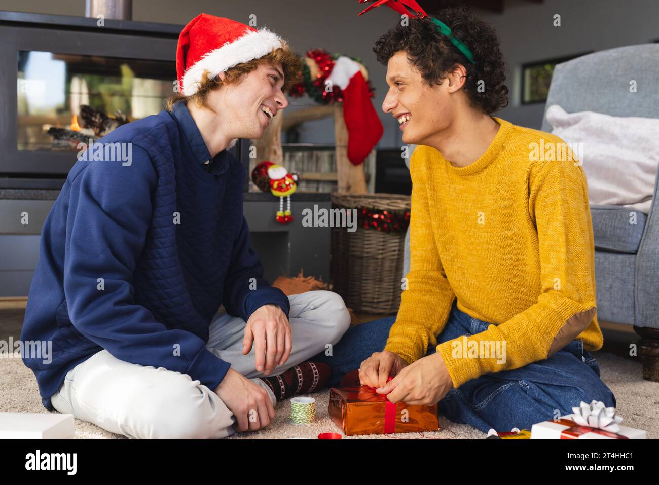 Heureux couple masculin gay diversifié portant des chapeaux de noël et des cadeaux d'emballage à la maison Banque D'Images