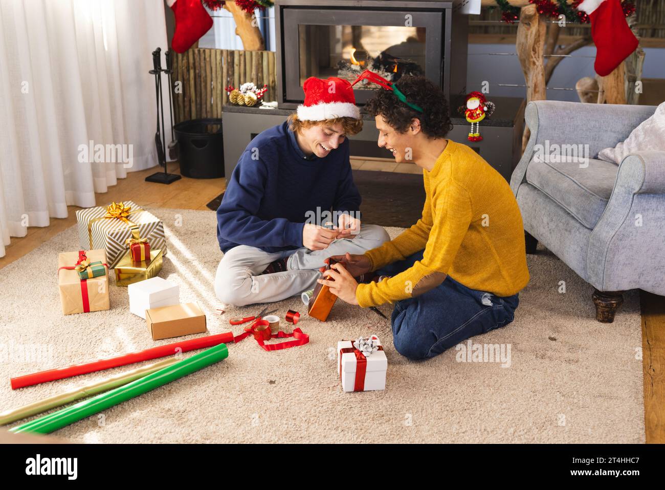 Heureux couple masculin gay diversifié portant des chapeaux de noël et des cadeaux d'emballage à la maison Banque D'Images