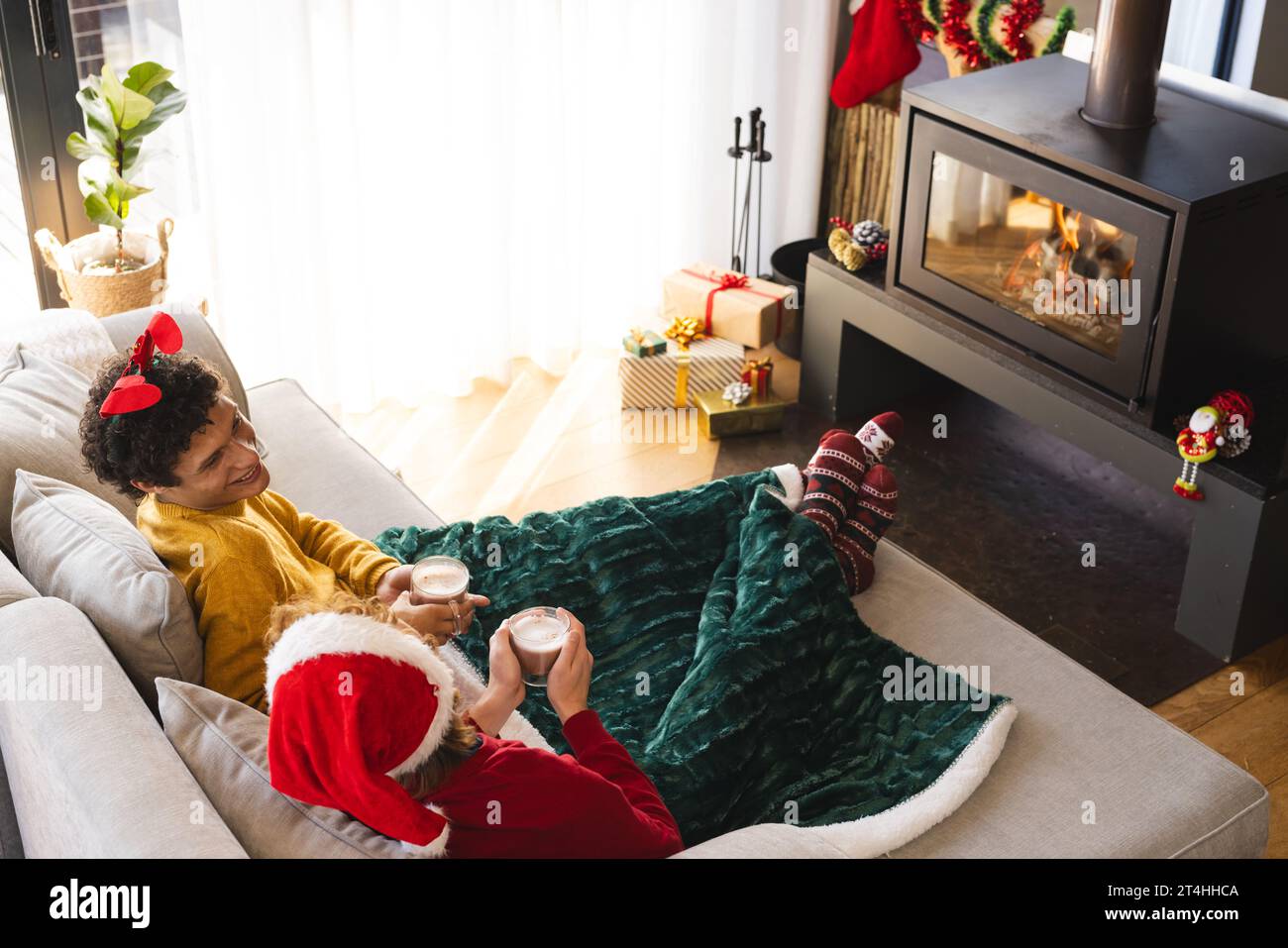 Heureux couple masculin gay diversifié buvant du cacao et portant des vêtements de noël à la maison Banque D'Images