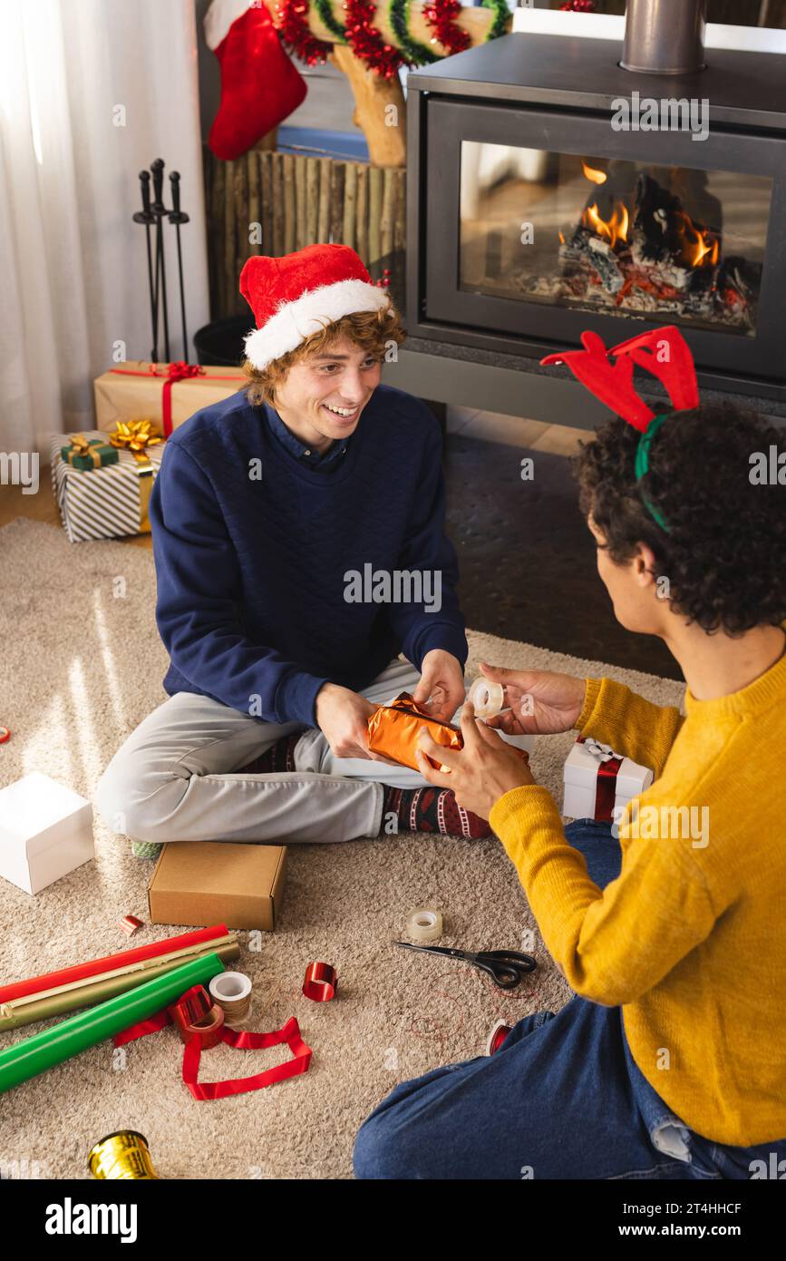 Heureux couple masculin gay diversifié portant des chapeaux de noël et des cadeaux d'emballage à la maison Banque D'Images