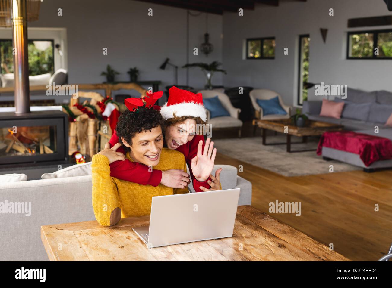 Heureux couple masculin gay diversifié embrassant porter des chapeaux de noël et ayant un appel vidéo à la maison Banque D'Images
