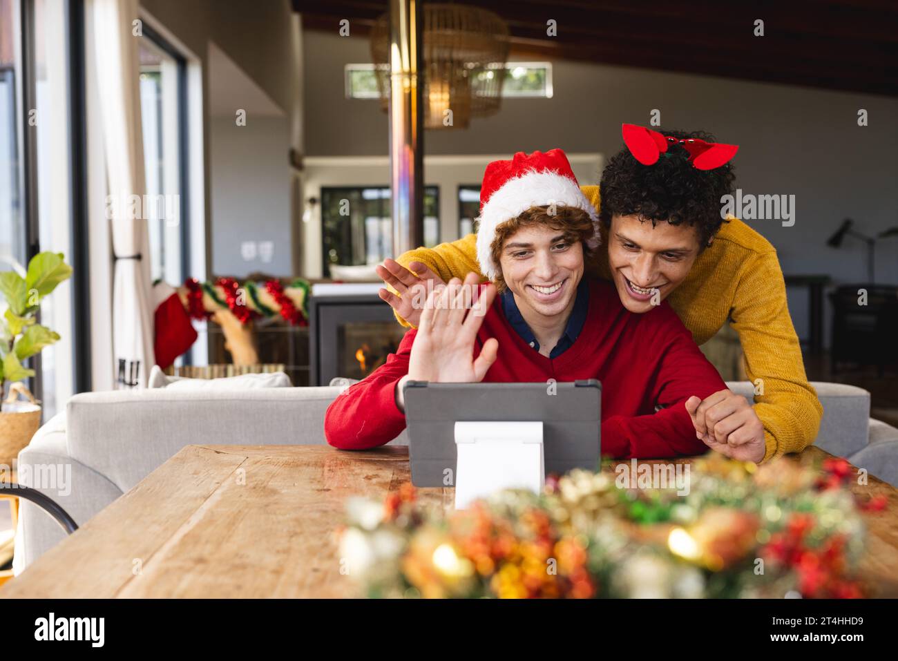 Heureux couple masculin gay diversifié embrassant porter des chapeaux de noël et ayant un appel vidéo à la maison Banque D'Images