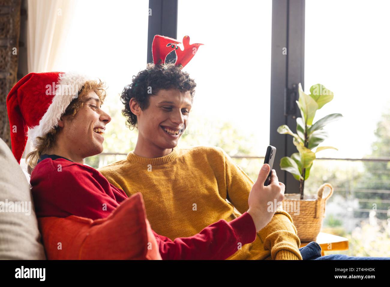 Heureux couple masculin gay diversifié embrassant porter des chapeaux de noël et ayant un appel vidéo à la maison Banque D'Images