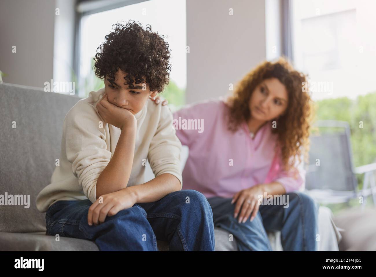 Garçon contrarié assis sur le canapé pendant que sa mère le regarde Banque D'Images