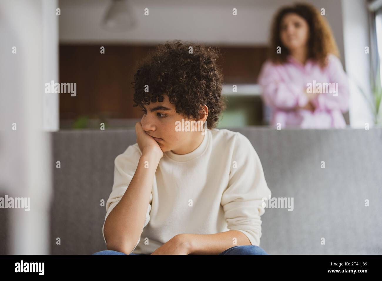 Garçon contrarié assis sur le canapé pendant que sa mère le regarde Banque D'Images