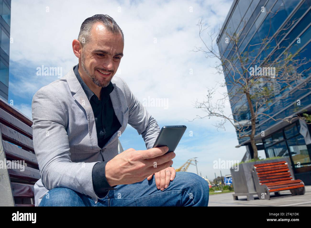 Homme adulte caucasien d'origine ethnique française et homme d'affaires, assis reposé à midi dehors heureux regarder le téléphone vérifier les médias sociaux et la notification Banque D'Images