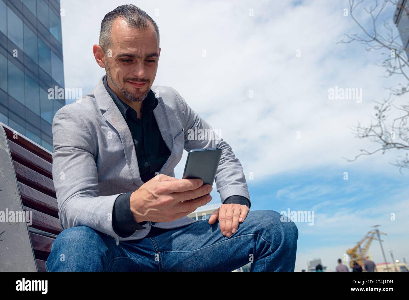 Homme adulte caucasien d'origine ethnique française et homme d'affaires, assis reposé à midi dehors heureux regarder le téléphone vérifier les médias sociaux et la notification Banque D'Images