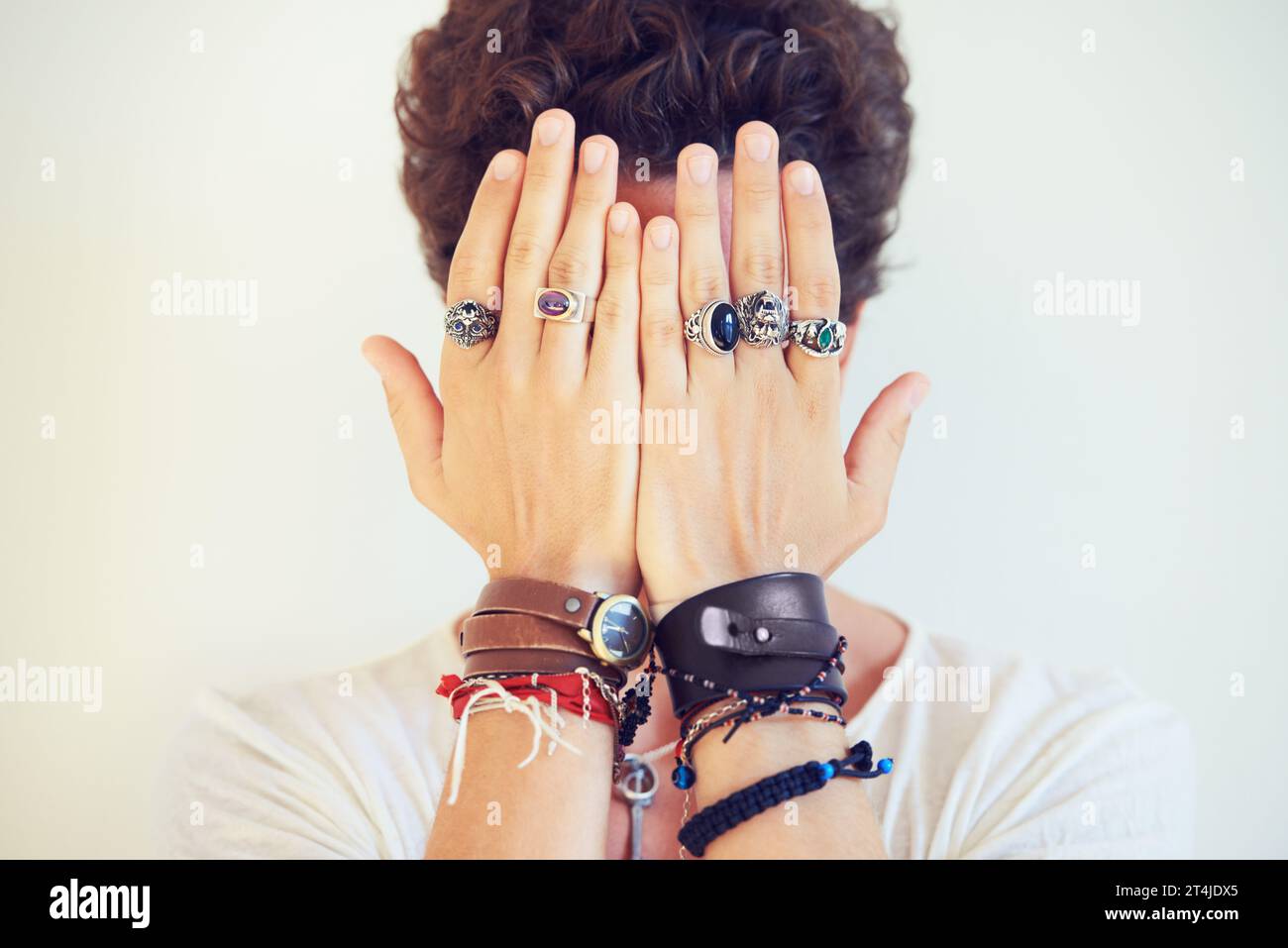 Mains, visage et couverture avec un homme en studio sur un fond blanc pour des accessoires de mode ou de style. Bijoux, bracelet et bagues sur les doigts d'un Banque D'Images