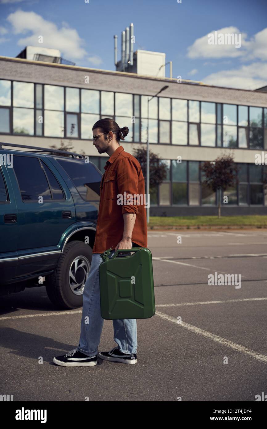 beau jeune homme en chemise marron avec un jean avec bidon d'essence à la main marchant vers sa voiture Banque D'Images