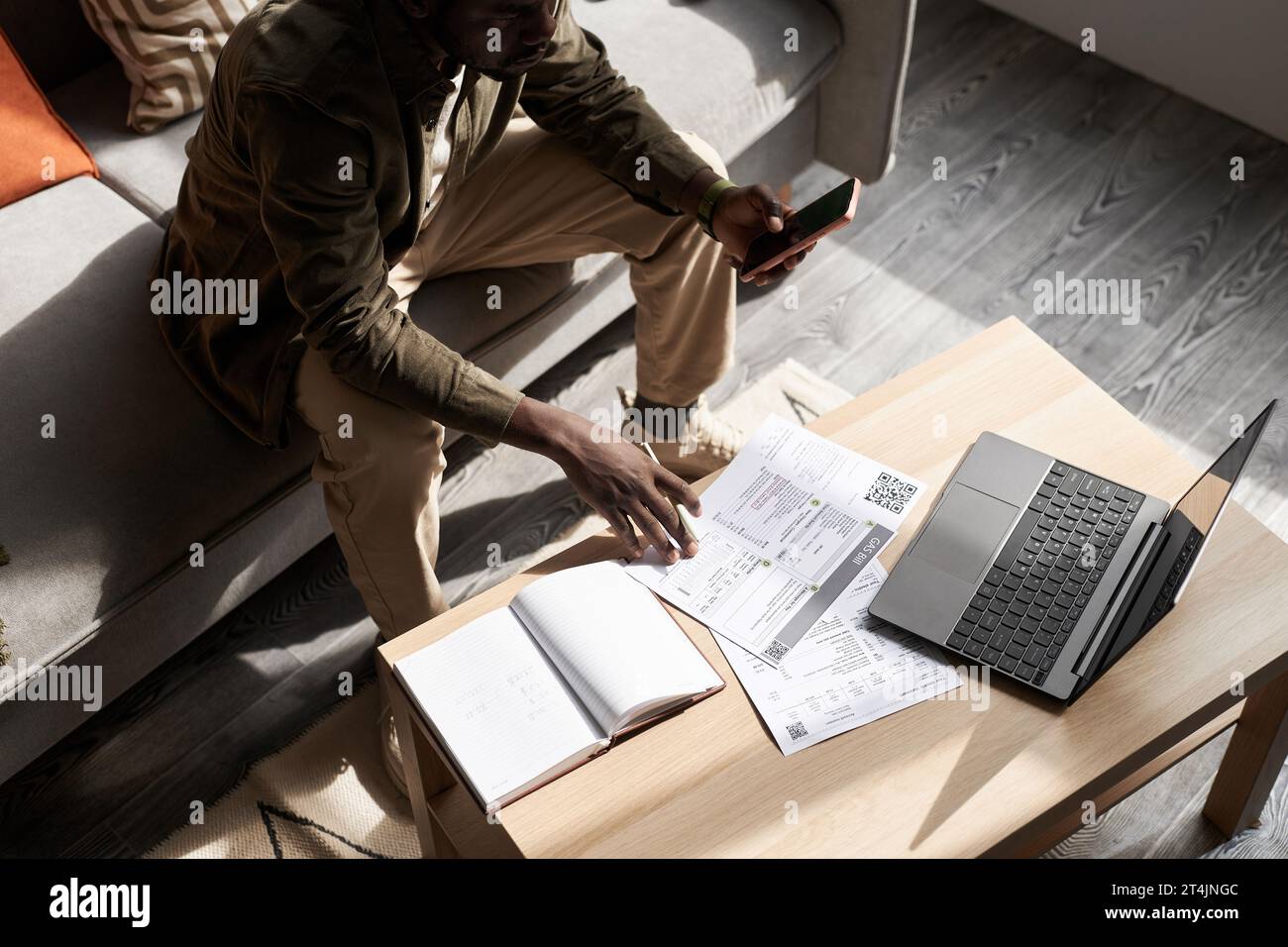 Portrait à grand angle de l'homme adulte noir faisant des impôts à la maison dans la lumière du soleil avec des documents financiers sur la table, espace de copie Banque D'Images