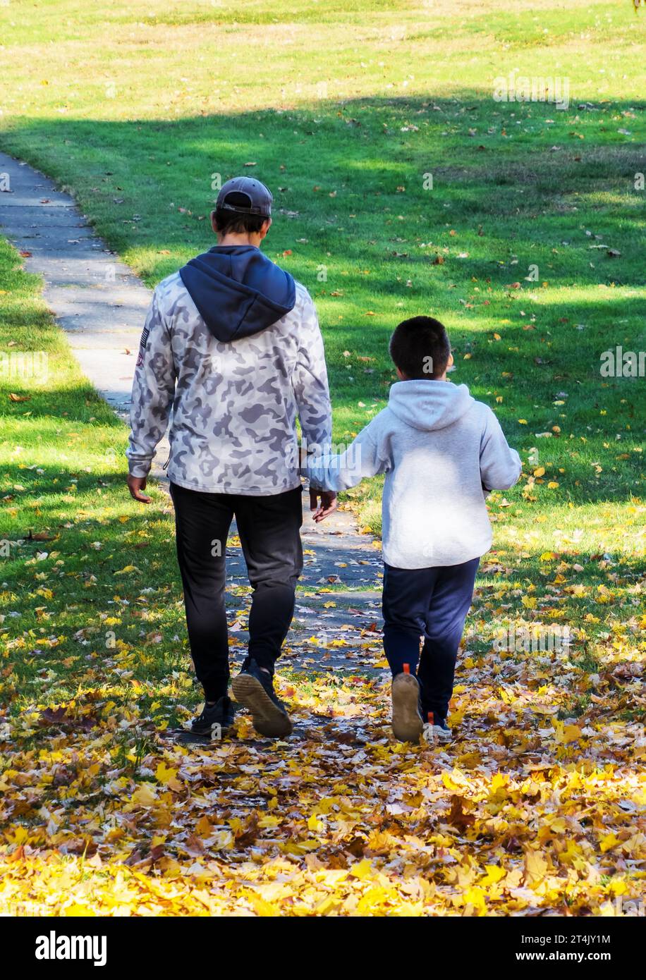 Père et fils se promènent parmi les feuilles d'automne. Banque D'Images