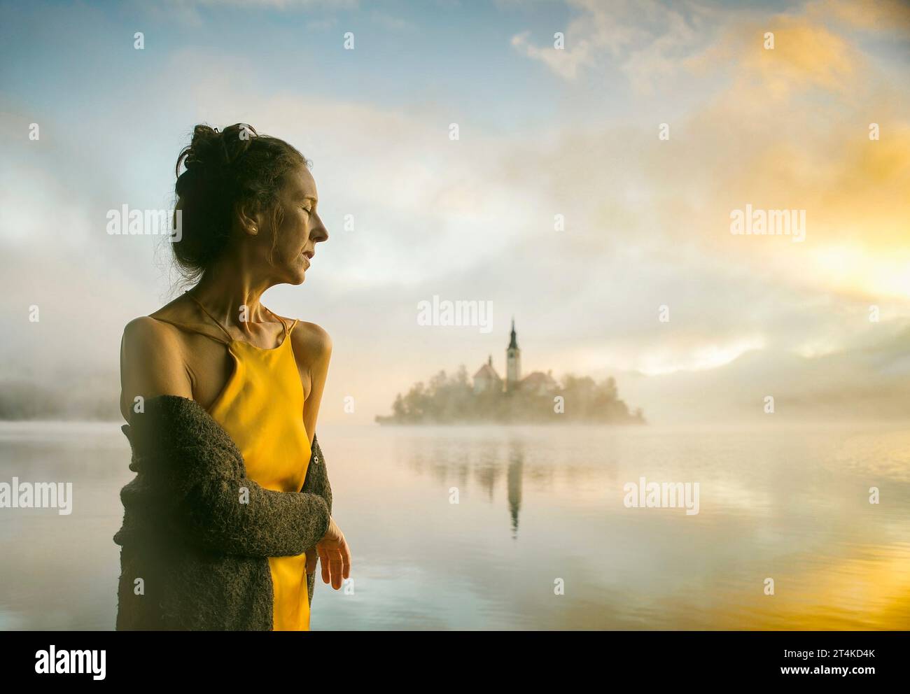 Femme en robe jaune regardant un lever de soleil parmi le brouillard sur les rives du lac de Bled, Slovénie Banque D'Images
