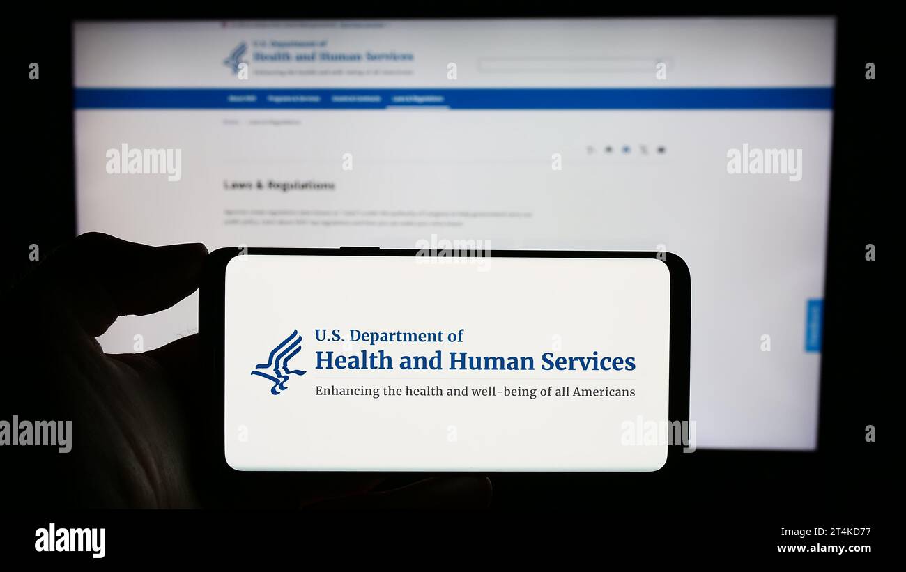 Personne tenant un téléphone portable avec le logo du ministère américain de la Santé et des Services sociaux (HHS) devant la page Web. Concentrez-vous sur l'affichage du téléphone. Banque D'Images
