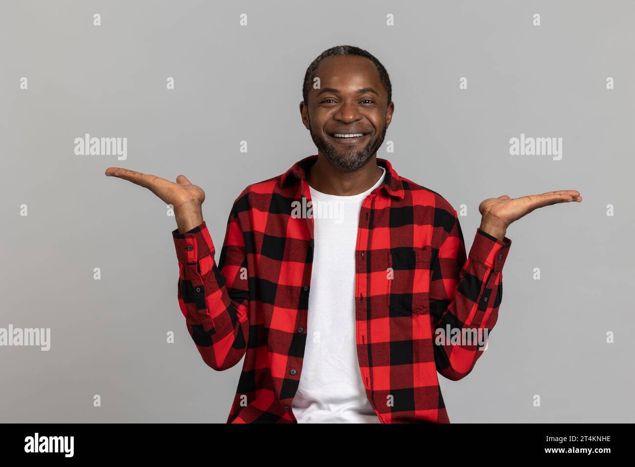 Joyeux homme barbu noir portant une chemise à carreaux rouge présentant un espace de copie sur les paumes Banque D'Images
