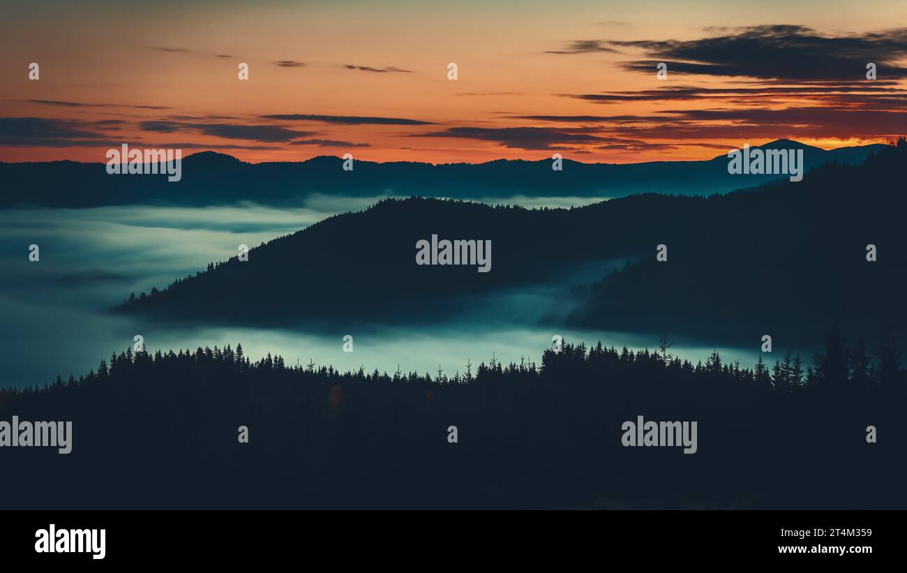 Lever de soleil mer de brouillard se déplaçant au-dessus de la chaîne de montagnes, silhouette de montagne des alpes avec vue aérienne de forêt de pins. Paysage brume de nature sauvage. Des nuages sombres dramatiques flottent dans le ciel de couleur orange Banque D'Images