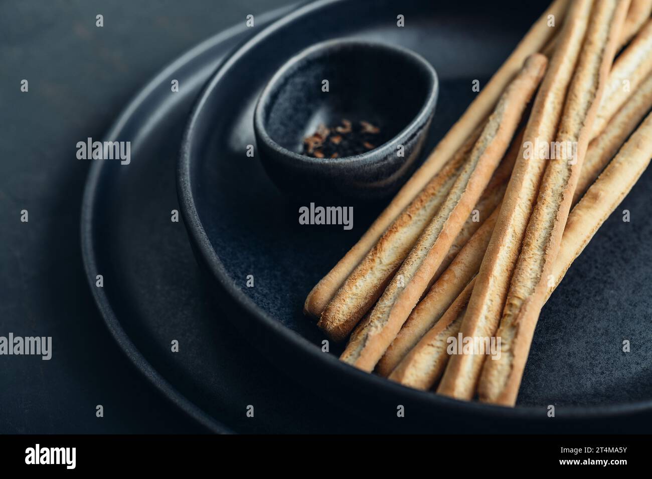 Grissini italiens frais cuits au four sur l'assiette avec des graines de sésame et de lin sur fond noir closeup Banque D'Images