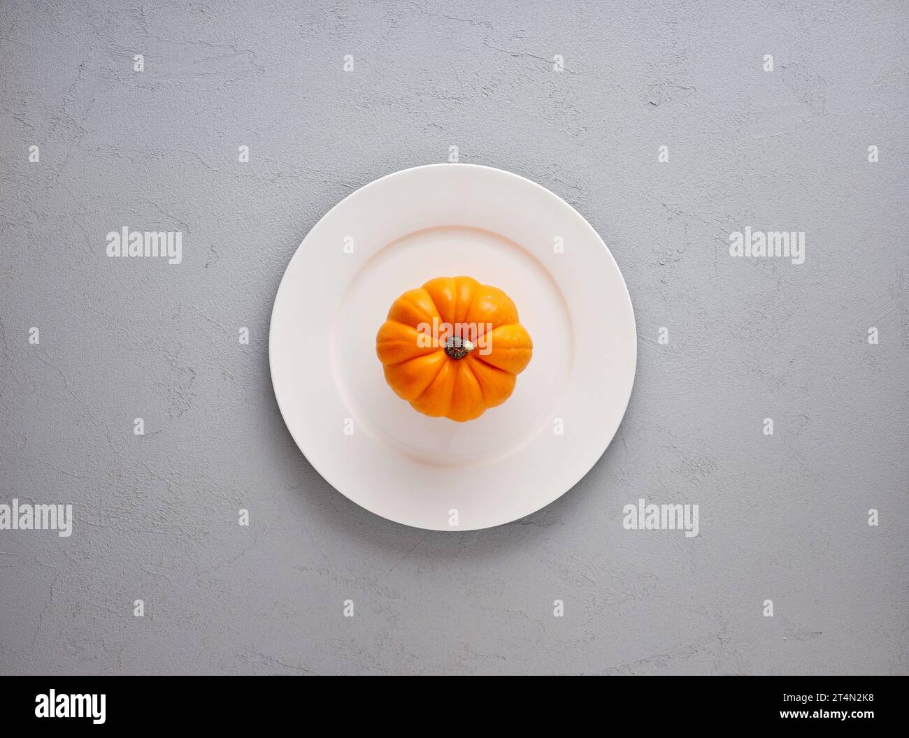 Citrouille d'automne de couleur orange sur une assiette blanche sur fond texturé gris avec espace de copie. Vue de dessus. Banque D'Images