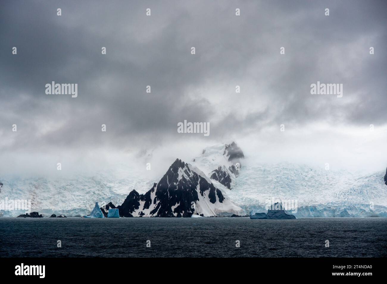 nuage bas au-dessus des montagnes couvertes de glace et de neige avec des icebergs flottant au premier plan. péninsule antarctique. antarctique Banque D'Images