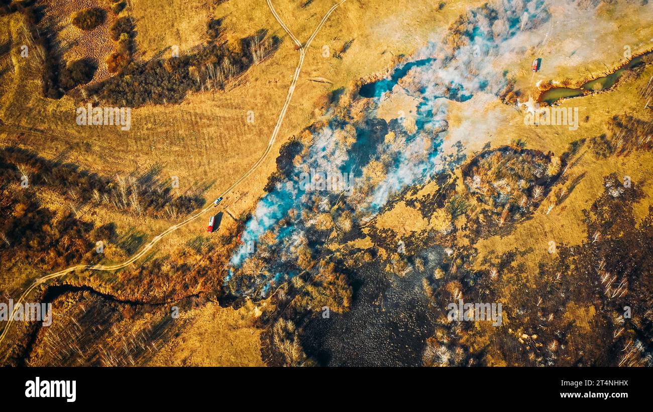 Vue aérienne. L'herbe sèche du printemps brûle pendant la sécheresse temps chaud. Feu et fumée de Bush. Moteur d'incendie, camion d'incendie en fonctionnement de lutte contre l'incendie. Feu sauvage Banque D'Images