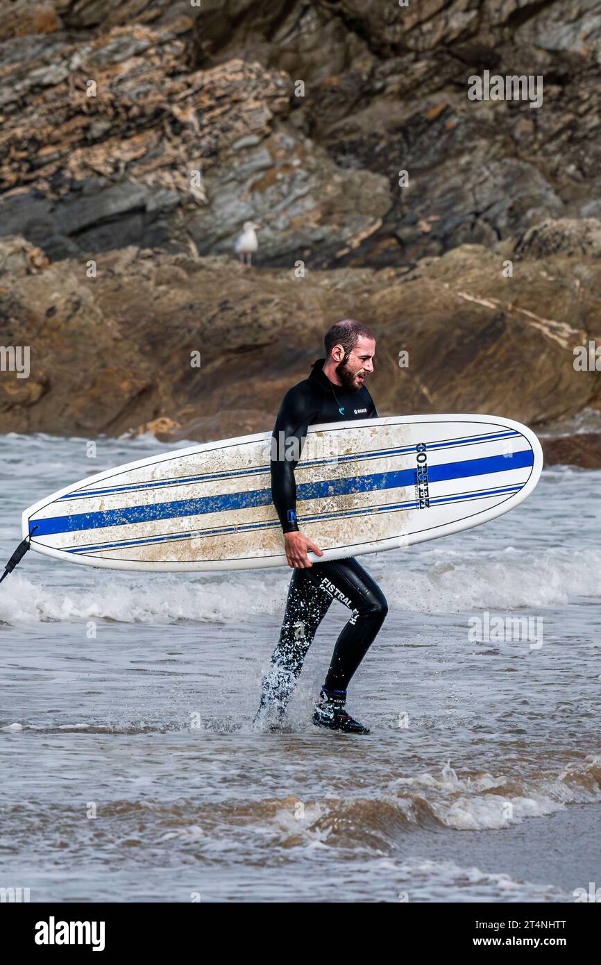 Un surfeur masculin fatigué portant sa planche de surf après une session de surf à Fistral à Newquay en Cornouailles au Royaume-Uni Banque D'Images