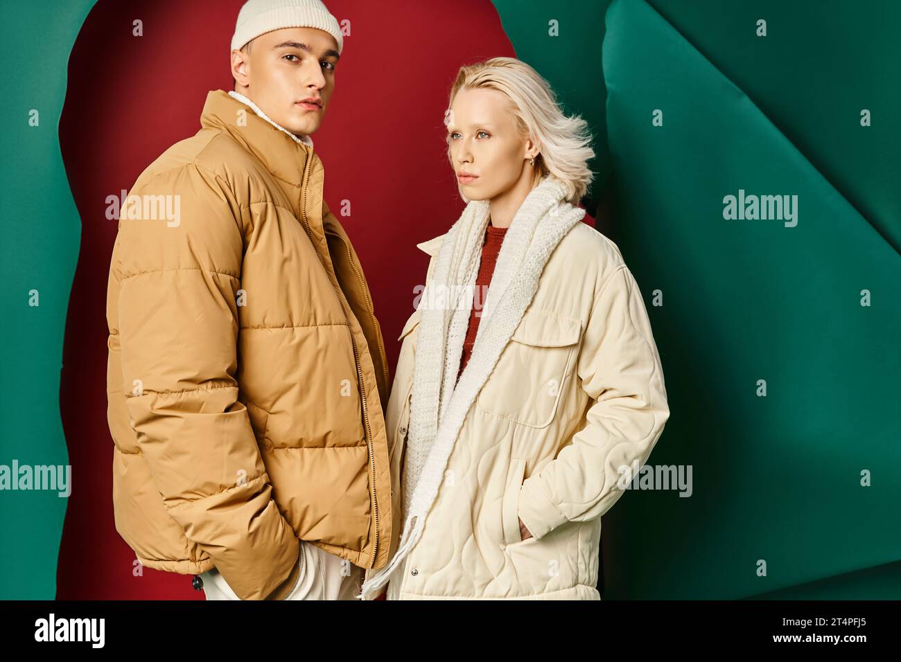 couple dans des vestes d'hiver à la mode posant avec les mains dans les poches sur fond rouge avec turquoise Banque D'Images