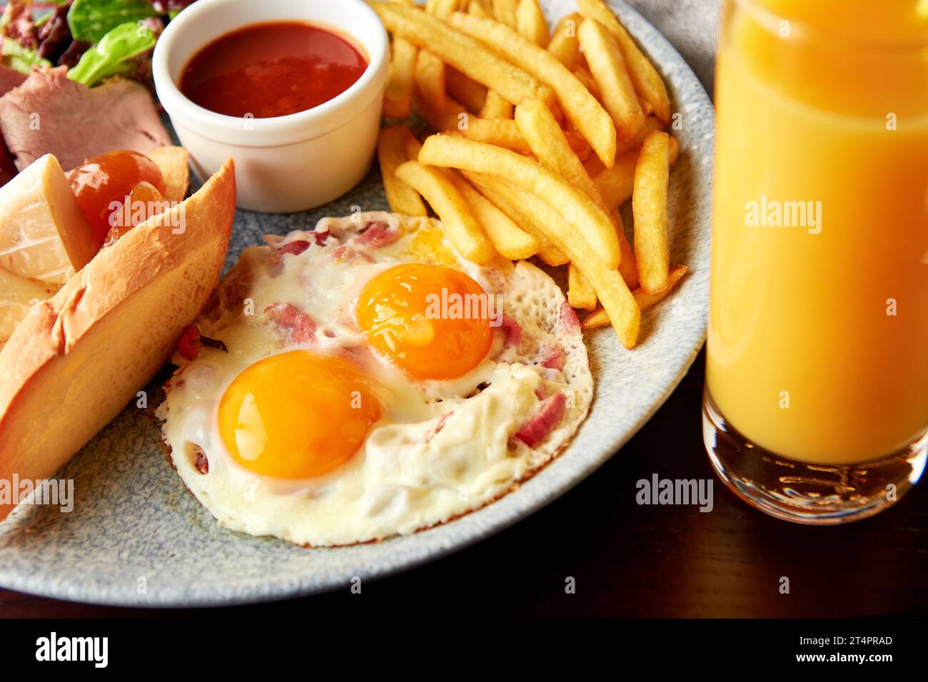 Petit-déjeuner anglais complet avec jambon, salade, œufs de caille frits avec bacon, pain grillé avec fromage et sauce tomate servis avec un verre de jus d'orange. Banque D'Images
