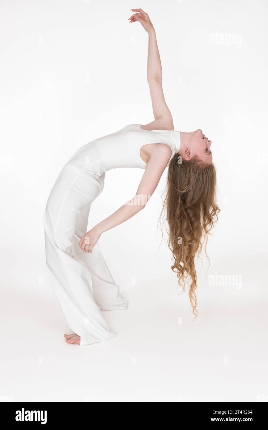 Vue en longueur d'une jeune danseuse flexible se penchant vers l'arrière avec les yeux fermés. Vue latérale du modèle pieds nus mince avec de longs cheveux ondulés Banque D'Images