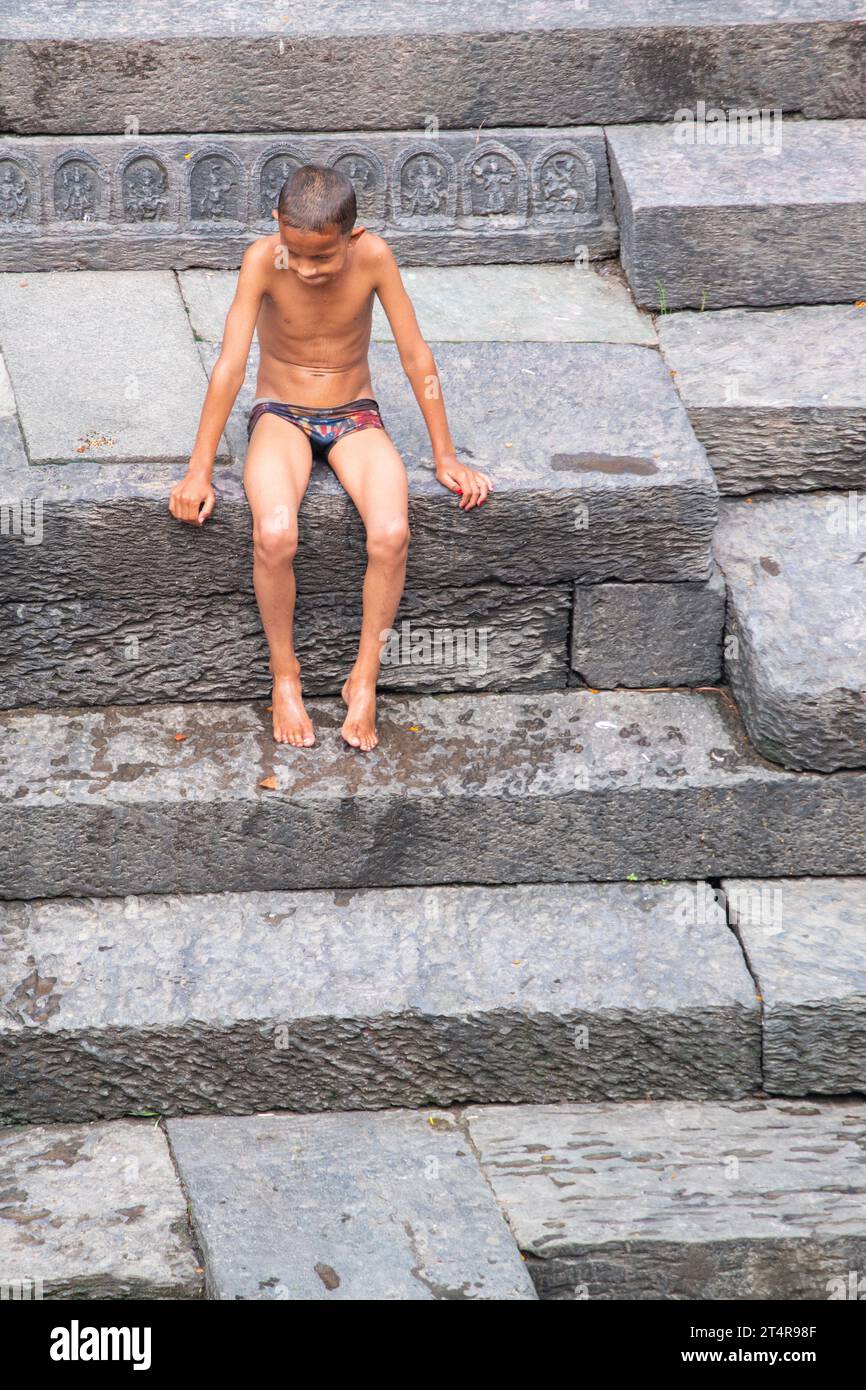 Katmandou, Népal : enfant hindou népalais se repose sur les escaliers après avoir plongé dans la rivière sacrée Bagmati, cérémonie de crémation au temple Pashupatinath, hindou Banque D'Images