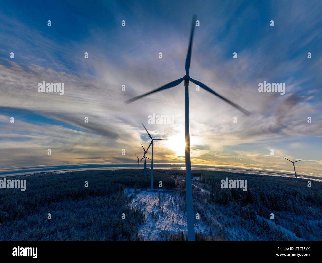 Vue panoramique aérienne sur le coucher du soleil sur Terre ronde, ligne d'horizon courbe avec la ferme de moulins à vent s'élevant au-dessus de la forêt de pins d'hiver, Suède du Nord. Banque D'Images