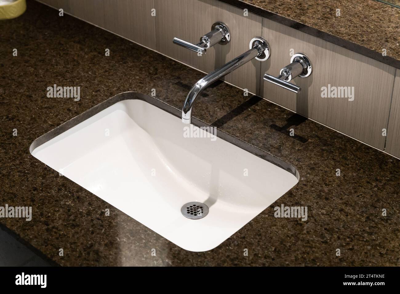 Un détail d'un lavabo de salle de bain d'en haut avec un robinet chromé poli, évier blanc, et un comptoir de granit brun. Banque D'Images