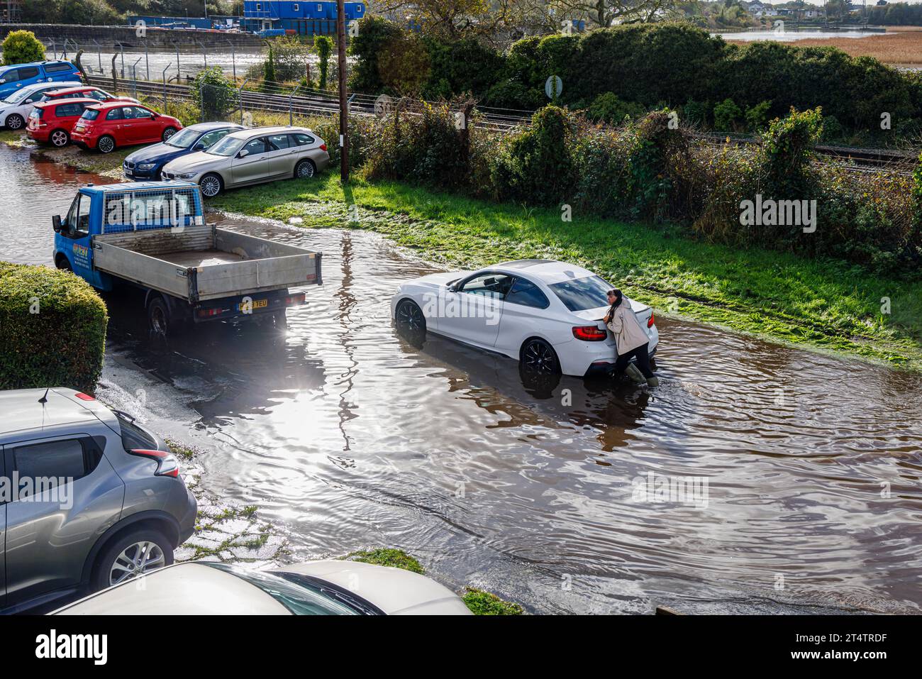 Une femme pousse une voiture BMW blanche en panne échouée sur une route inondée après de fortes pluies et une marée haute sur l'estuaire de la rivière Test à Southampton Banque D'Images