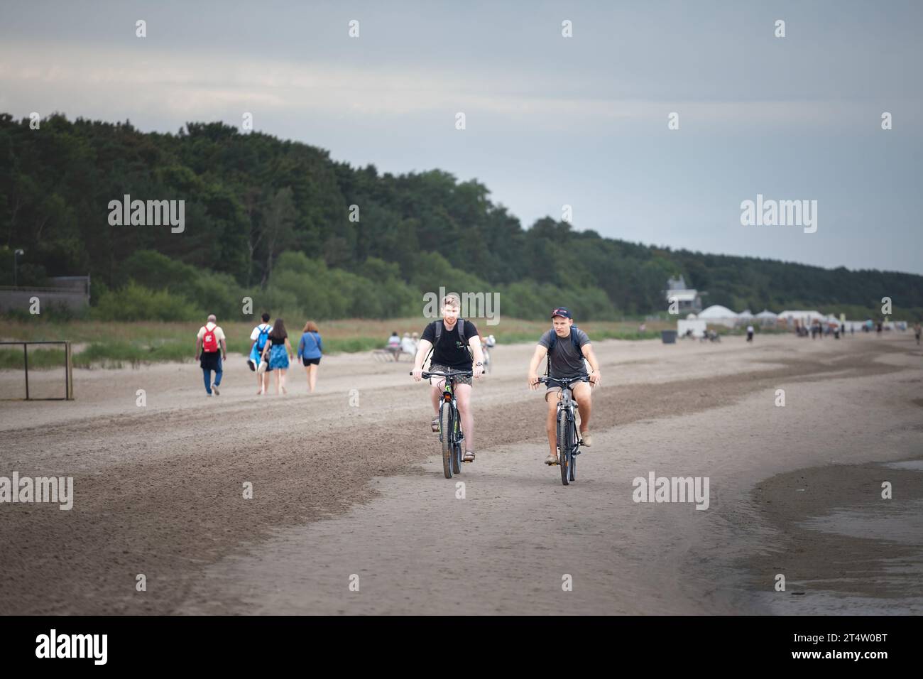 Photo de deux hommes conduisant des vélos sur le sable à Jurmala, sur une plage. Le Segway est une marque déposée de Segway Inc. Dean Kamen a inventé deux... Banque D'Images