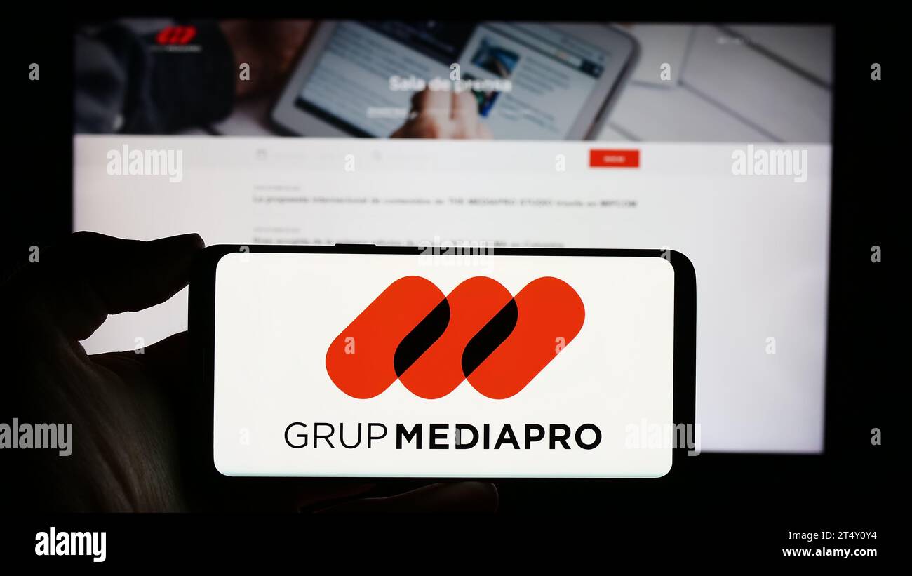 Personne tenant le téléphone portable avec le logo de la société multimédia espagnole Mediapro Group en face de la page Web de l'entreprise. Concentrez-vous sur l'affichage du téléphone. Banque D'Images