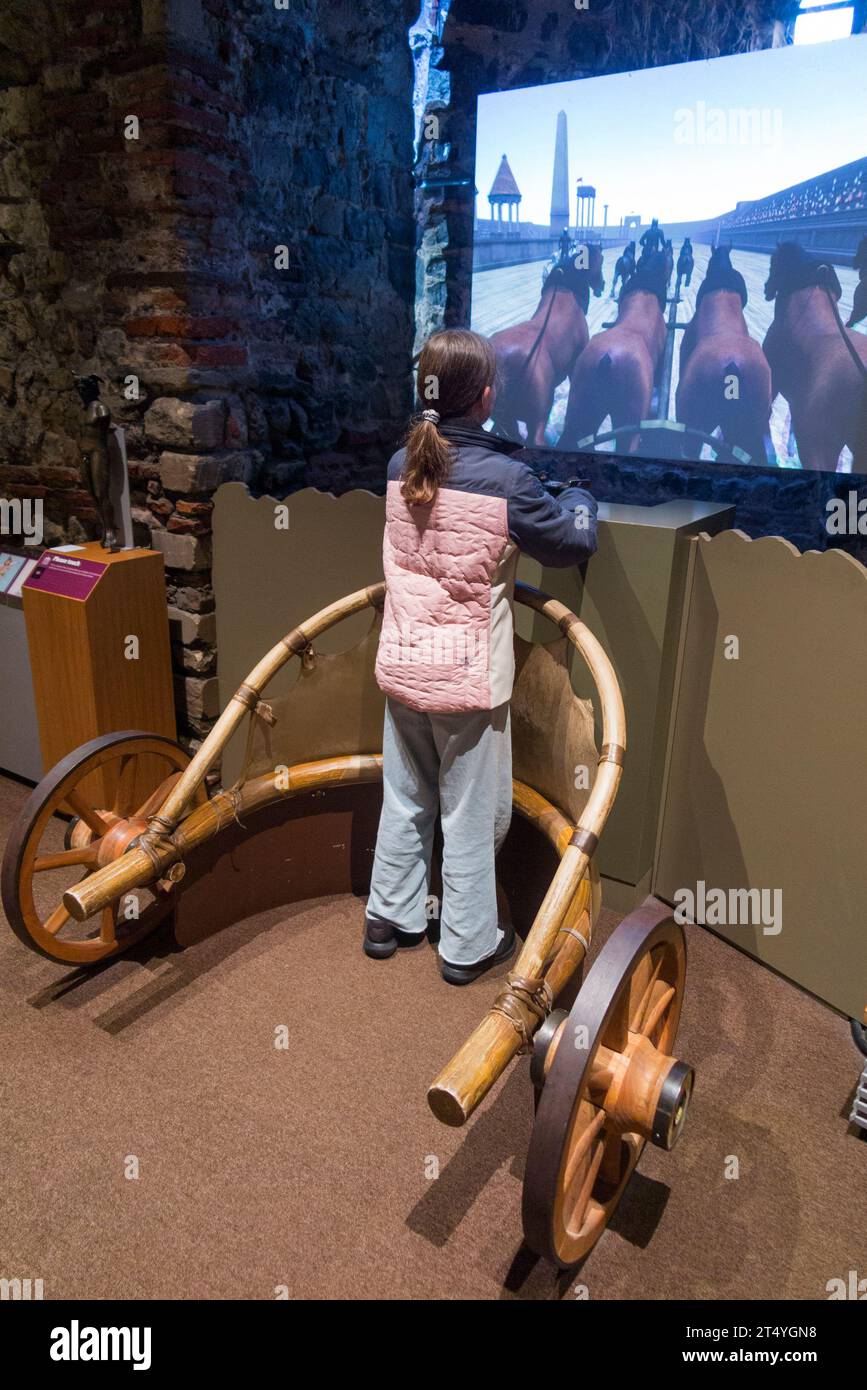 Enfant fille visiteur de musée jouant à l'écran de jeu vidéo romain interactif, pratiquant son défi de compétence de conduite de char. Château de Colchester Royaume-Uni (136) Banque D'Images