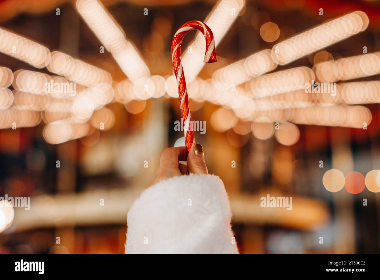Détails magiques des vacances de Noël. Mains féminines tenant la sucette douce canne blanche rouge sur le fond de guirlande lumineuse dorée. Banque D'Images