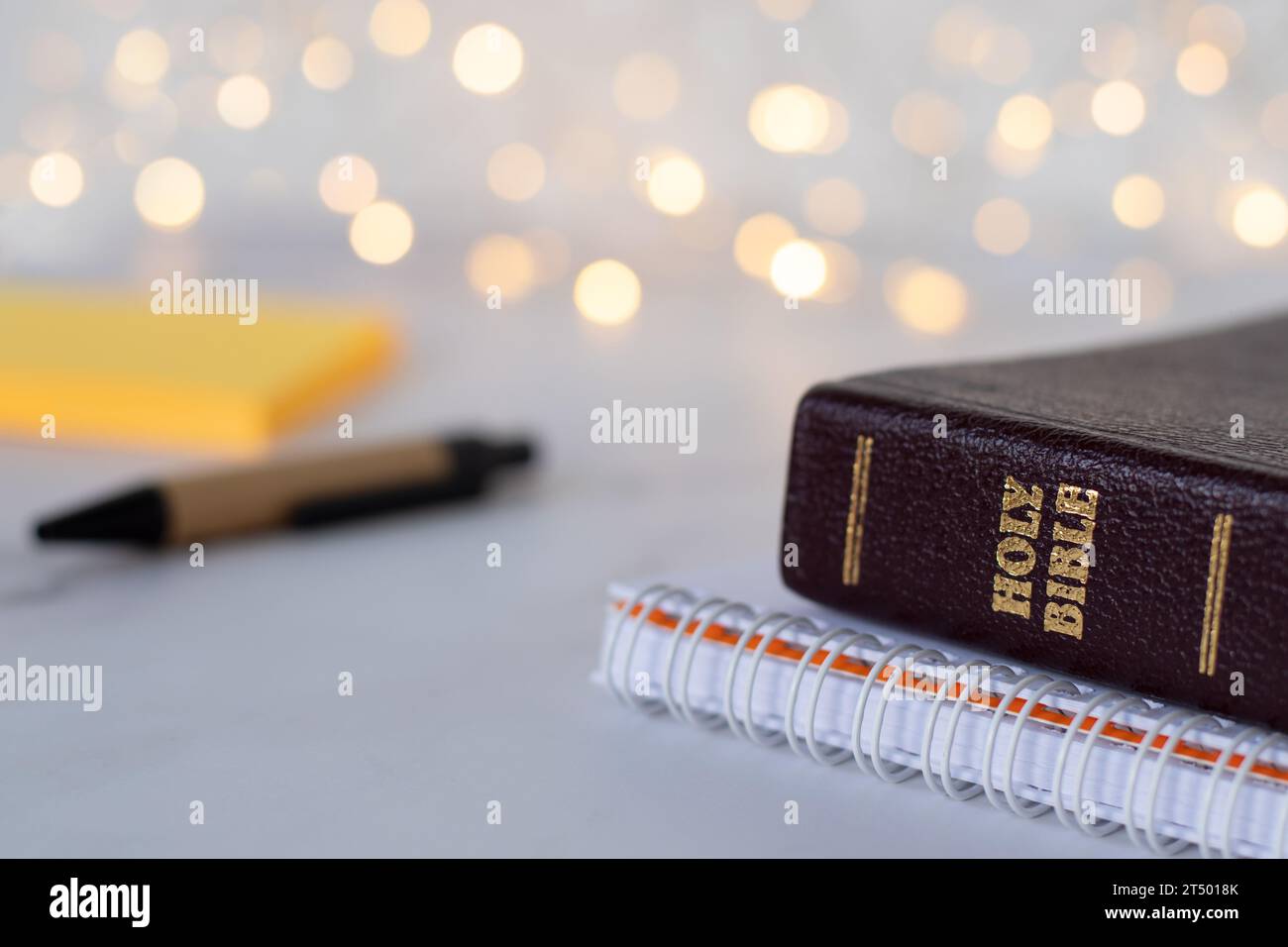 Gros plan du livre sacré de la bible avec texte de lettre d'or avec cahier en spirale, stylo et notes avec fond bokeh flou. Étudier les Écritures chrétiennes. Banque D'Images