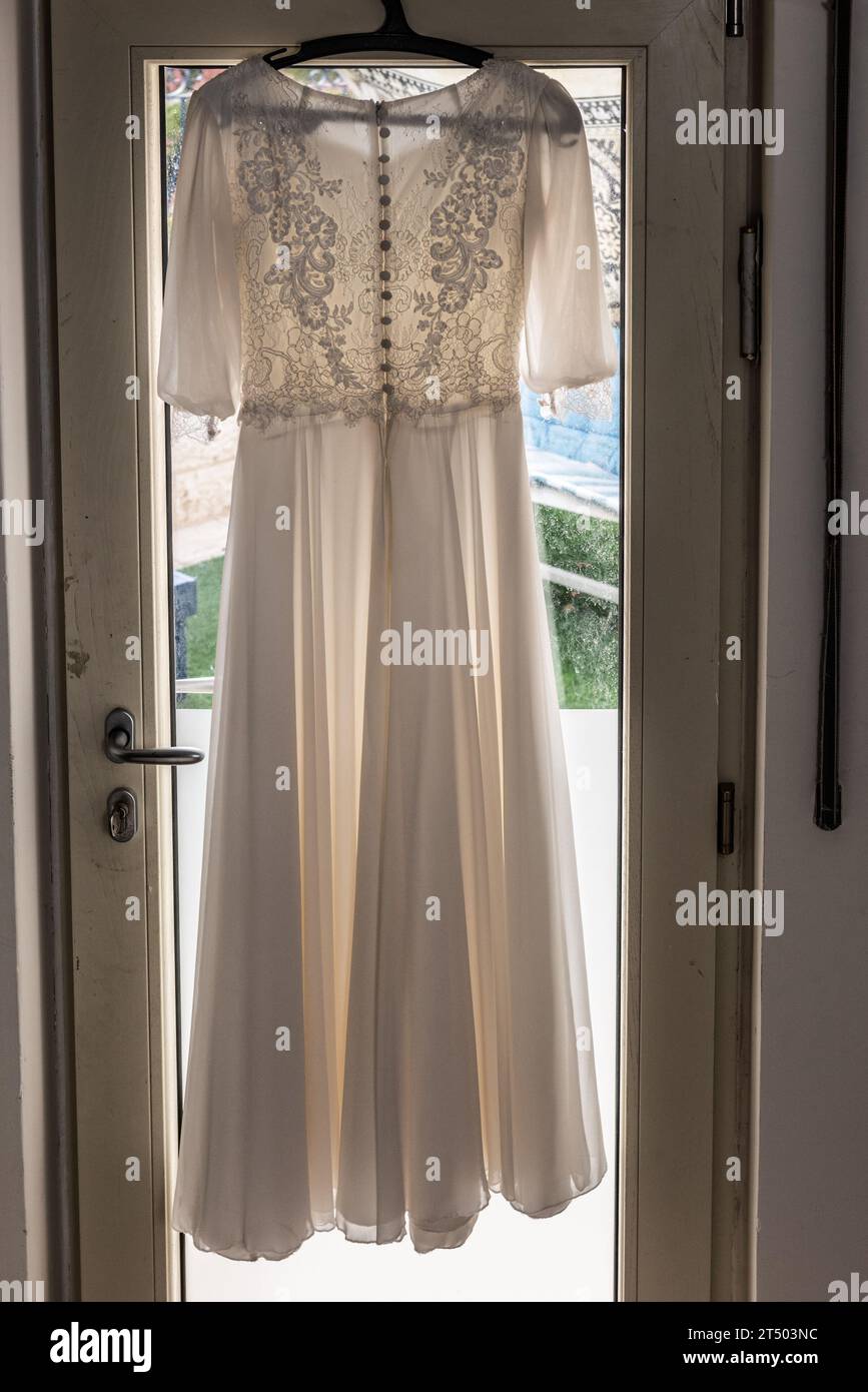 Une robe de mariée à motif et dentelle blanche pend au-dessus d'une porte avant une cérémonie de mariage. Banque D'Images