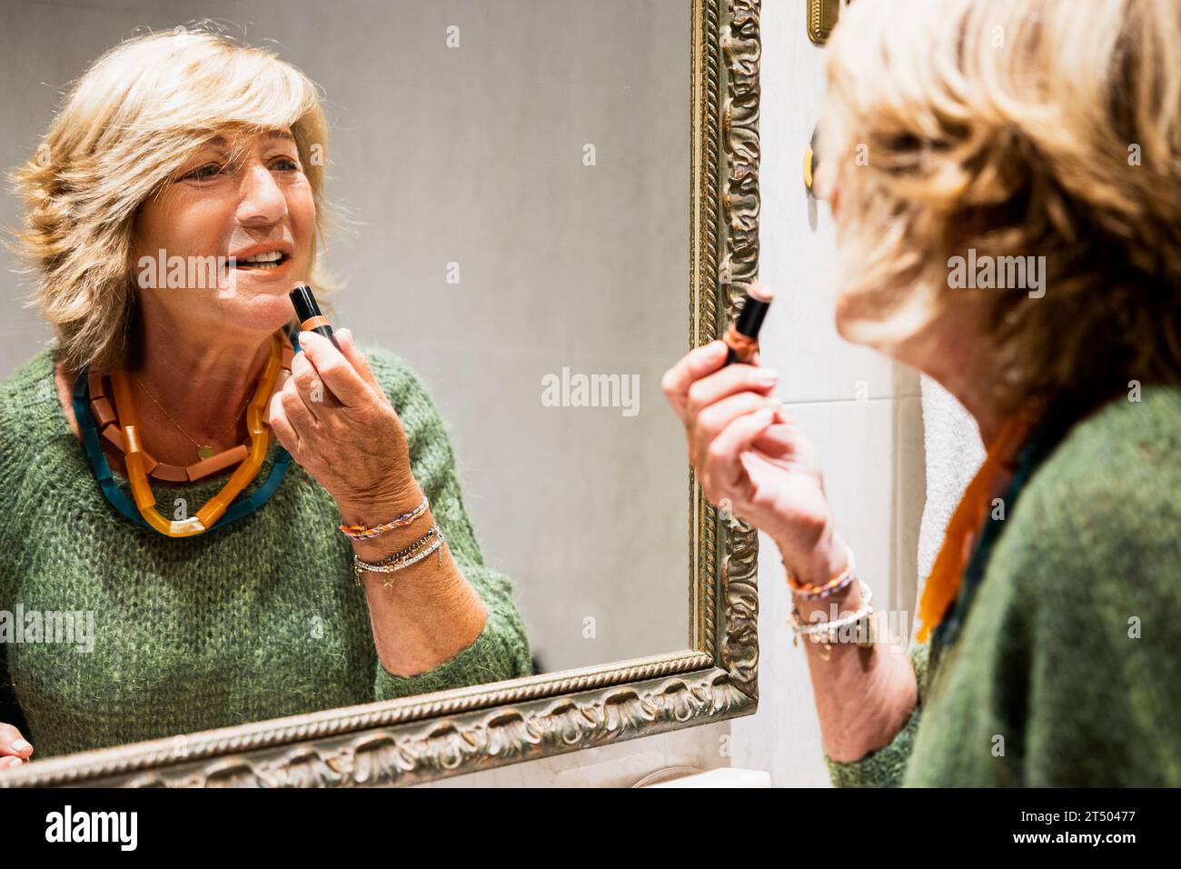 Femme mature se maquillant les lèvres devant le miroir de la salle de bain Banque D'Images