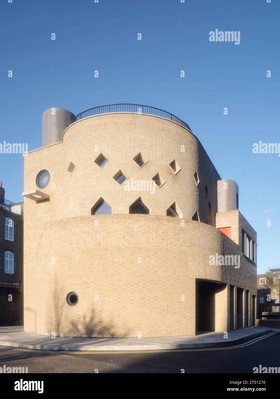 Façade en briques éclairée par le soleil avec fenêtres circulaires et en forme de losange. The Hoxton Mule - Ivy Street, Londres, Royaume-Uni. Architecte : Sam Jacob Studio, 2022. Banque D'Images