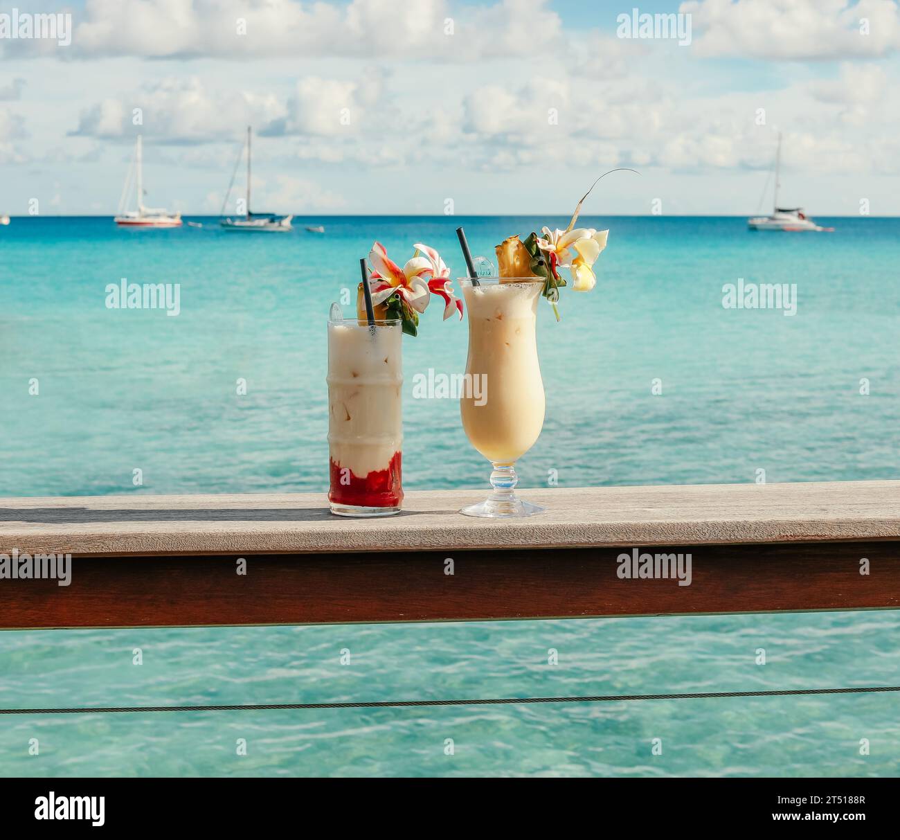Deux boissons glacées avec garnitures florales sur le rebord d'un quai surplombant le magnifique océan turquoise avec des voiliers au loin Banque D'Images
