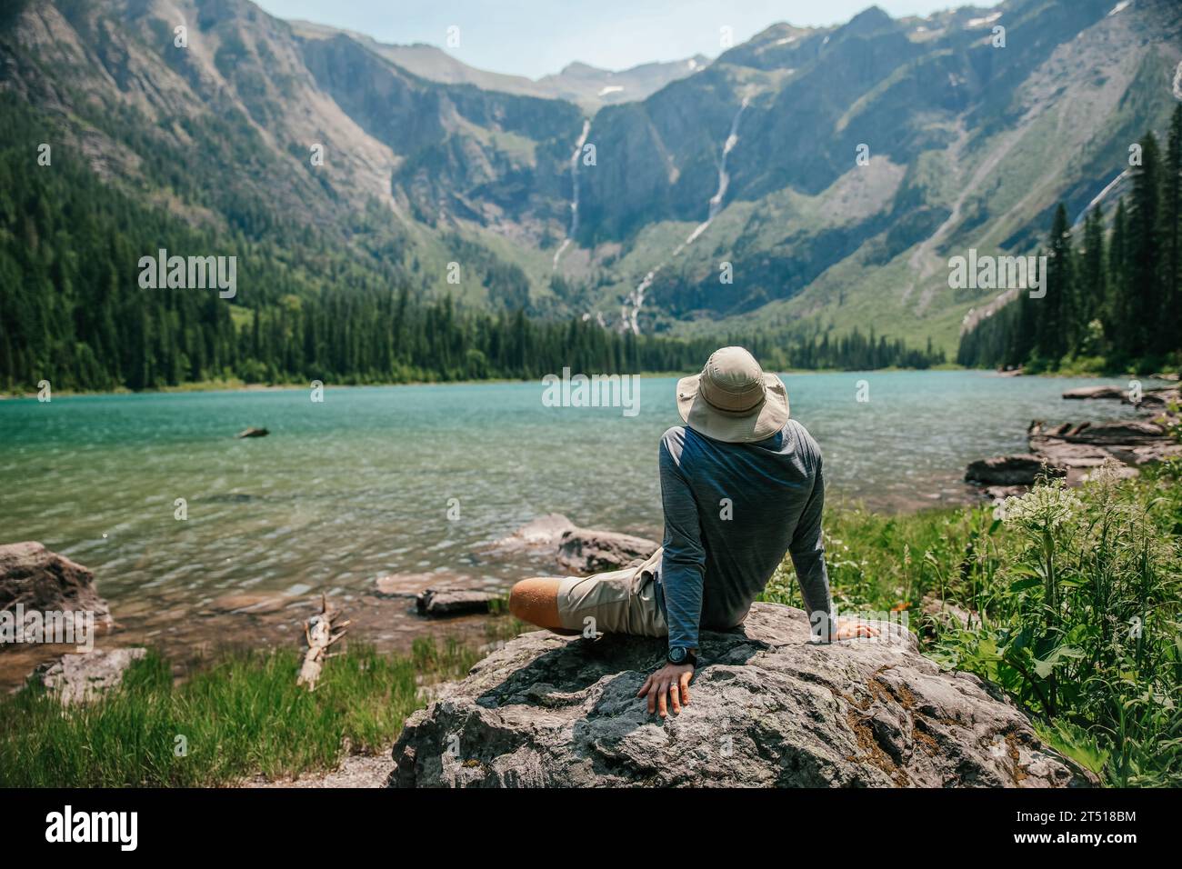 L'homme est assis admirant le lac alpin en face de lui avec de multiples cascades au loin Banque D'Images