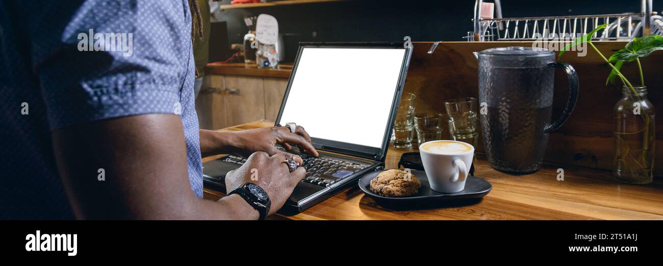 bannière de l'homme d'affaires noir méconnaissable, debout travaillant avec son ordinateur portable à l'intérieur du restaurant, tout en prenant un café avec cookie, affaires freelance c Banque D'Images